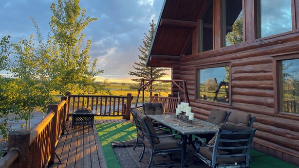 A wooden cabin with a deck, outdoor seating, and large windows.