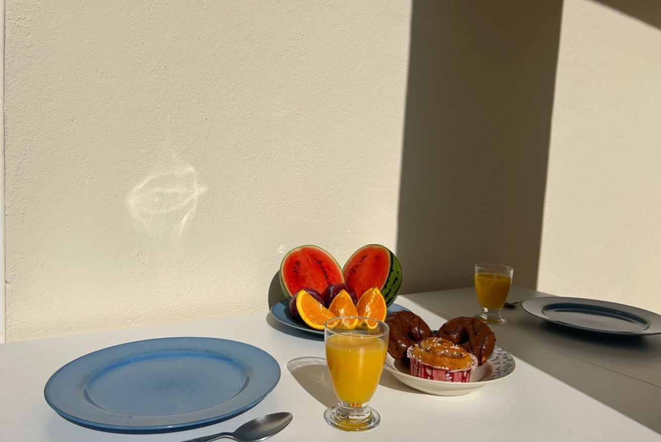 A breakfast table with plates, a glass of orange juice, a plate of pastries, and a watermelon.