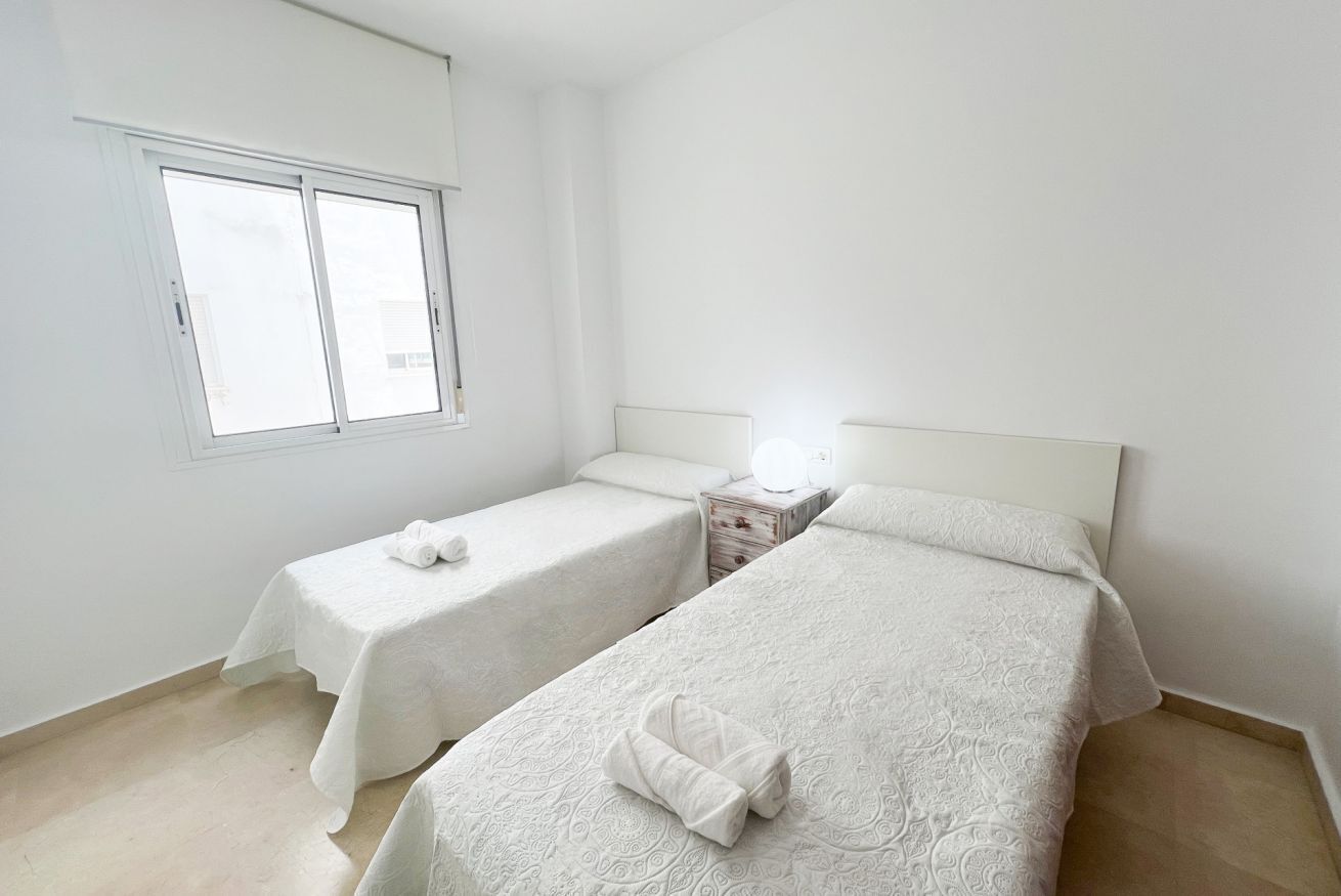 A room with two beds, a window, and a bedside table with a lamp.