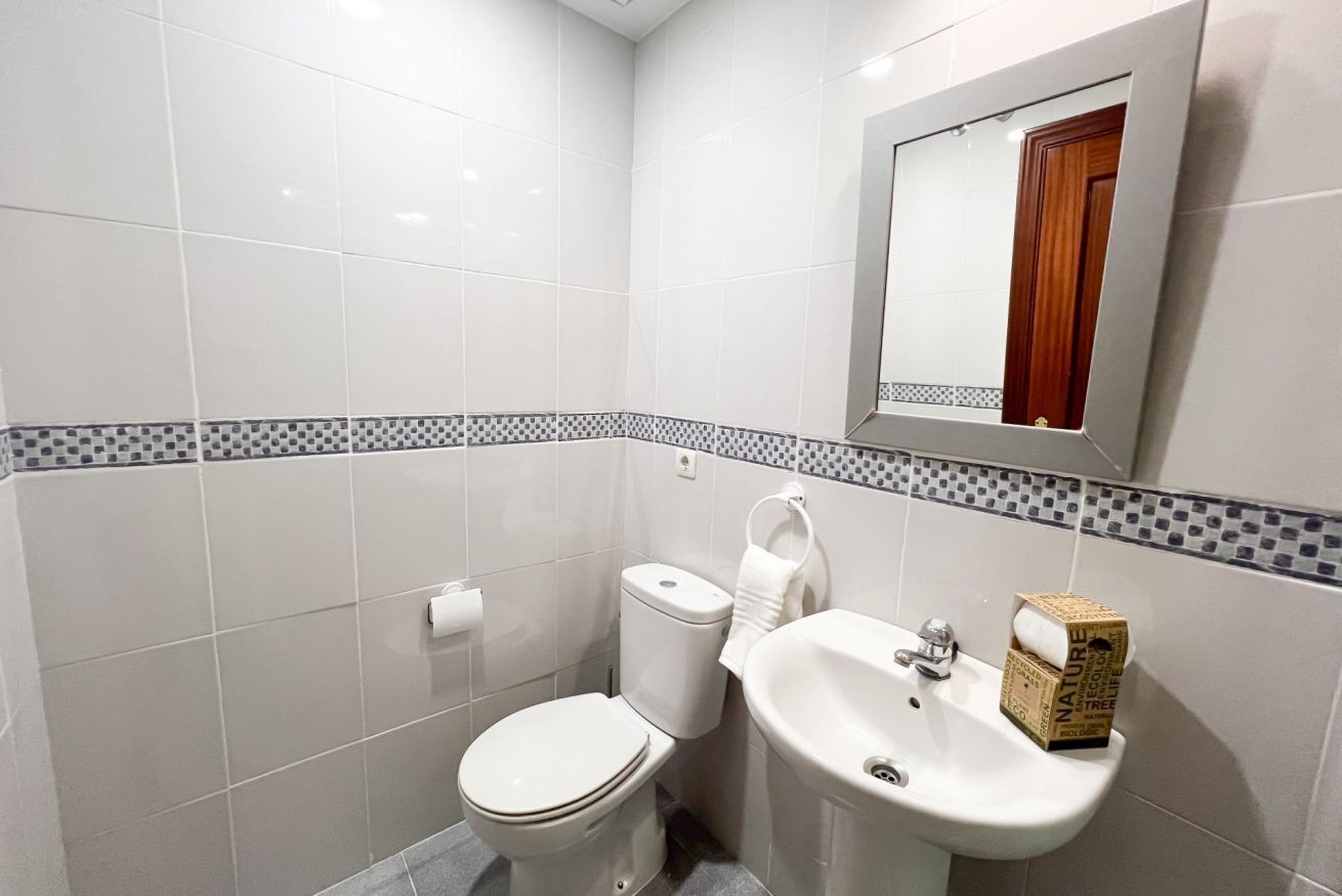 A small bathroom with white tiles, a toilet, a sink, and a mirror.