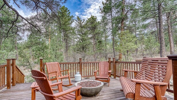 A wooden deck with Adirondack chairs and a fire pit, surrounded by a forest.