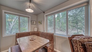 A room with a wooden bench seating area, large windows with forest views, and framed pictures on the walls.