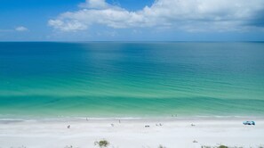 Uma praia com águas turquesa cristalinas, areia branca e algumas pessoas e guarda-sóis.