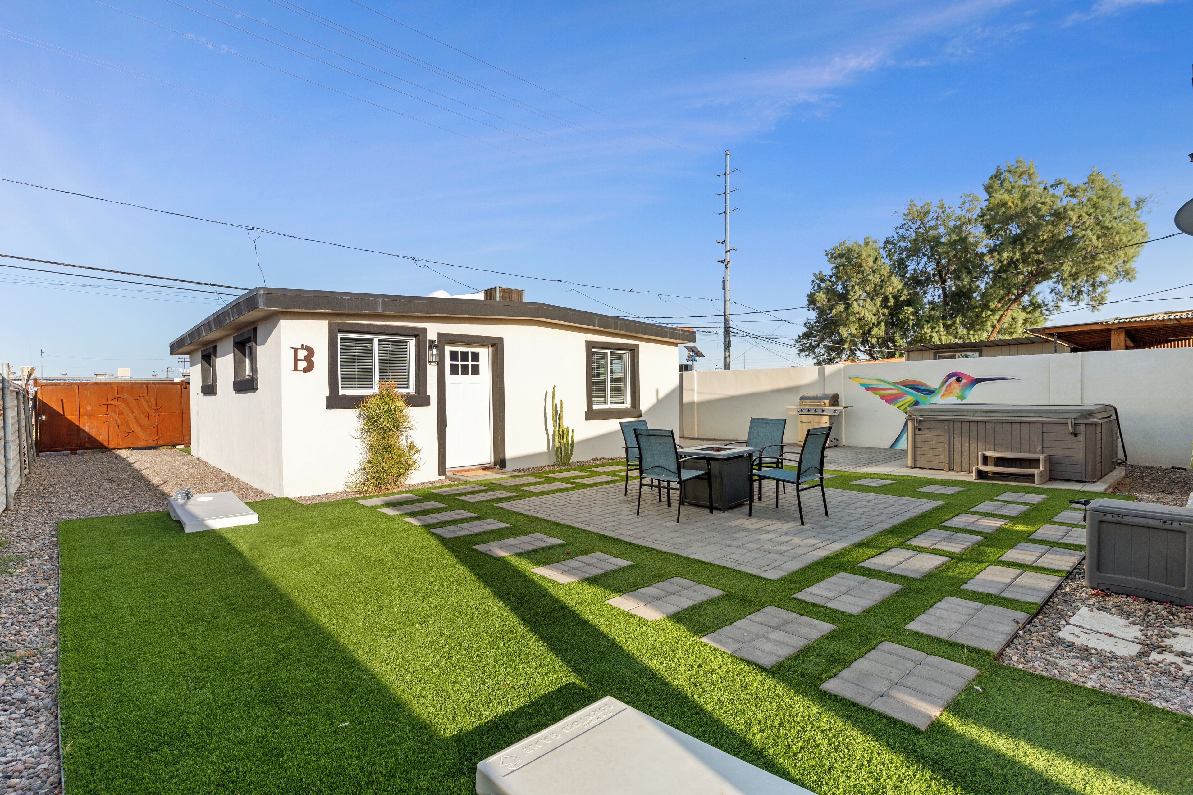 A backyard with artificial grass, a patio with chairs and a table, and a hot tub.
