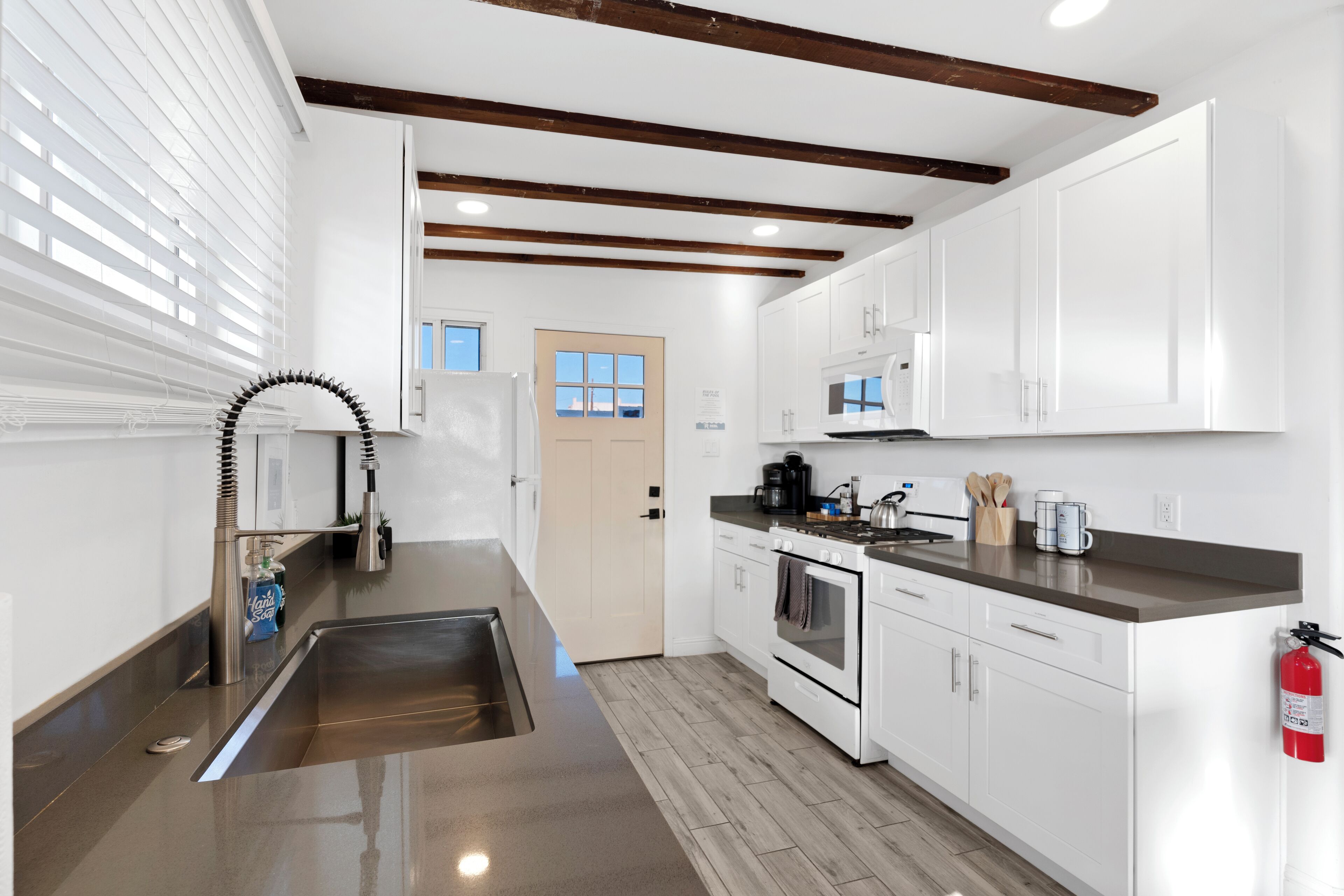 A modern kitchen with white cabinets, a stainless steel sink, and a wooden ceiling.