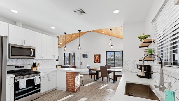 Una cocina moderna con armarios blancos, horno empotrado, microondas y un comedor con mesa y sillas.