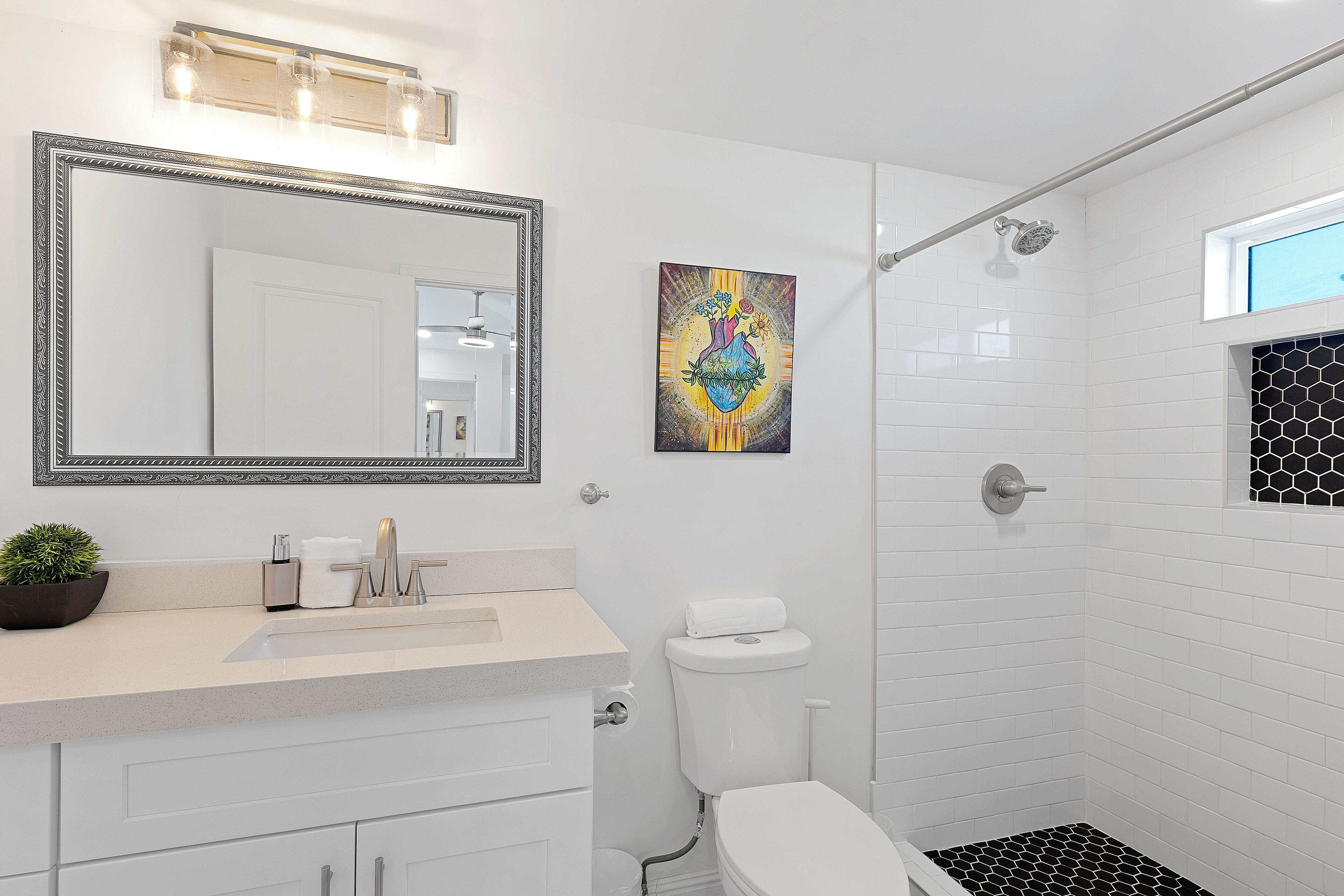 Un baño con un espejo grande, un lavamanos con planta en maceta, inodoro y ducha.