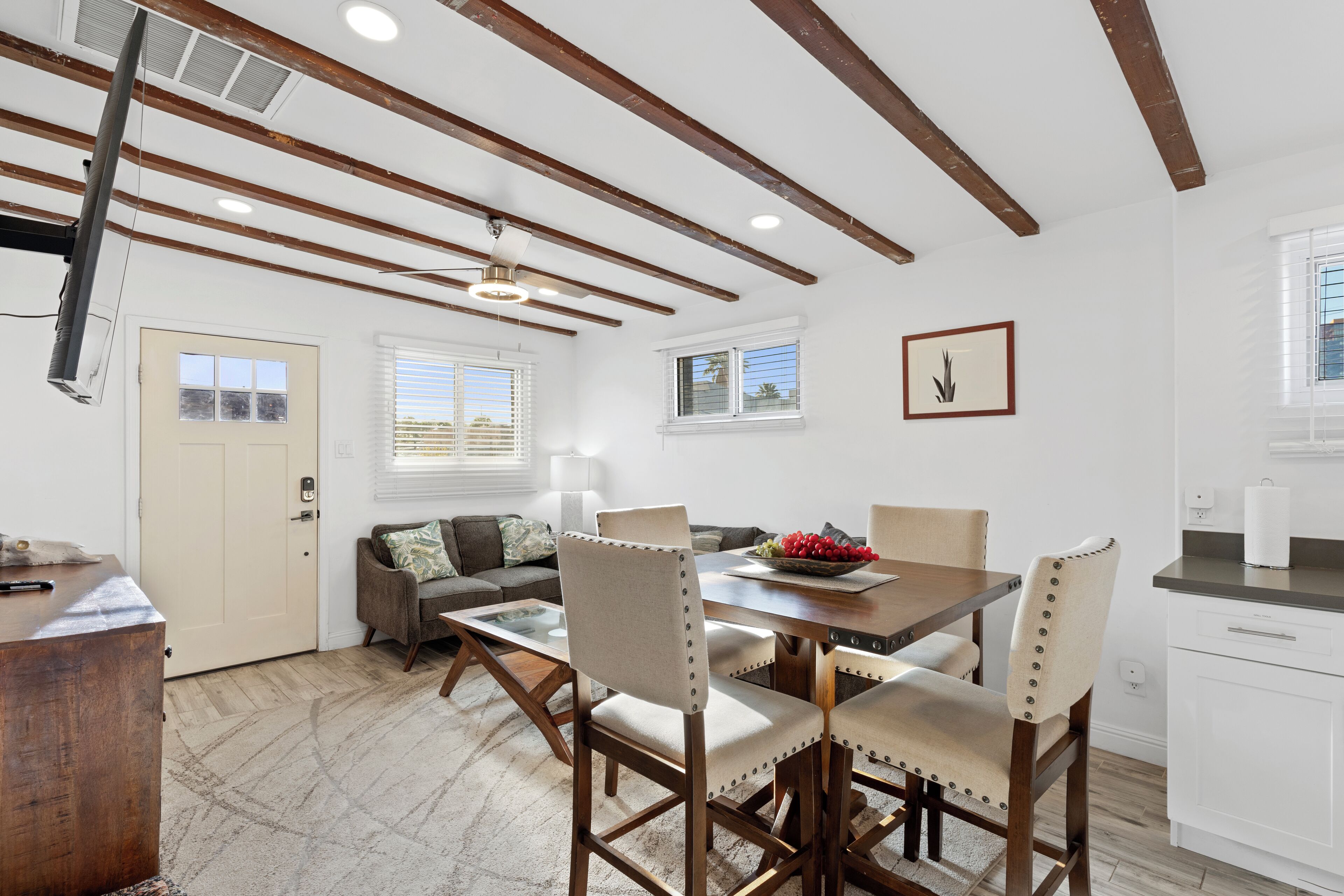 A dining area with a wooden table and chairs, a ceiling fan, and a view of the outside through windows.