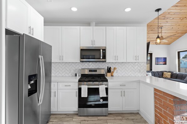 A modern kitchen with white cabinets, stainless steel appliances, and a brick accent wall. - Cottage with BBQ & Hot Tub (Phoenix)
