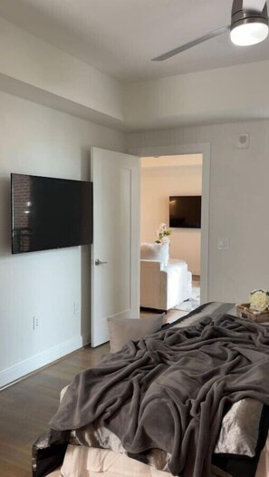 A bedroom with a bed, a TV mounted on the wall, and a ceiling fan.