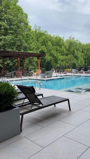 A pool area with a pergola, lounge chairs, and potted plants.