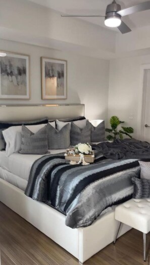 A modern bedroom with a large bed, a ceiling fan, and two framed artworks on the wall.