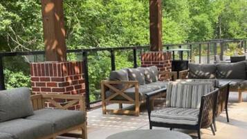 Een terras buiten met houten meubels, een stenen open haard en een pergola.