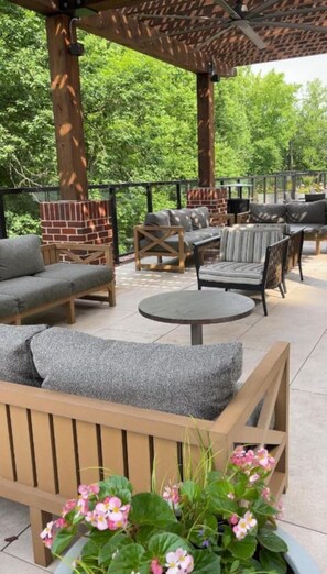 An outdoor patio with wooden furniture, a brick fireplace, and a pergola.
