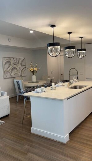 A modern kitchen with a central island, pendant lighting, and a dining area with a vase of flowers.