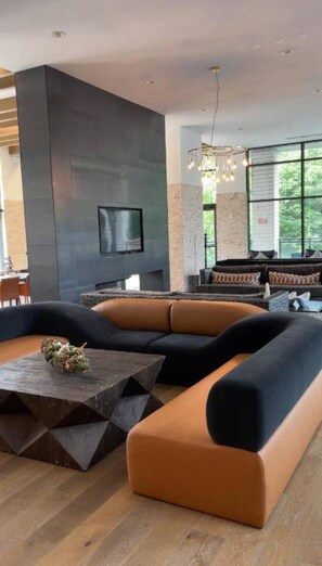 A modern living room with a sectional sofa, a coffee table, and a large window providing a view of greenery outside. - Buckhead Atlanta Luxury Suite (Atlanta)