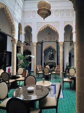 An interior with a central seating area, surrounded by ornate arches and columns, featuring a patterned floor and a chandelier. - Riad Dar Lalzohra (Rabat)