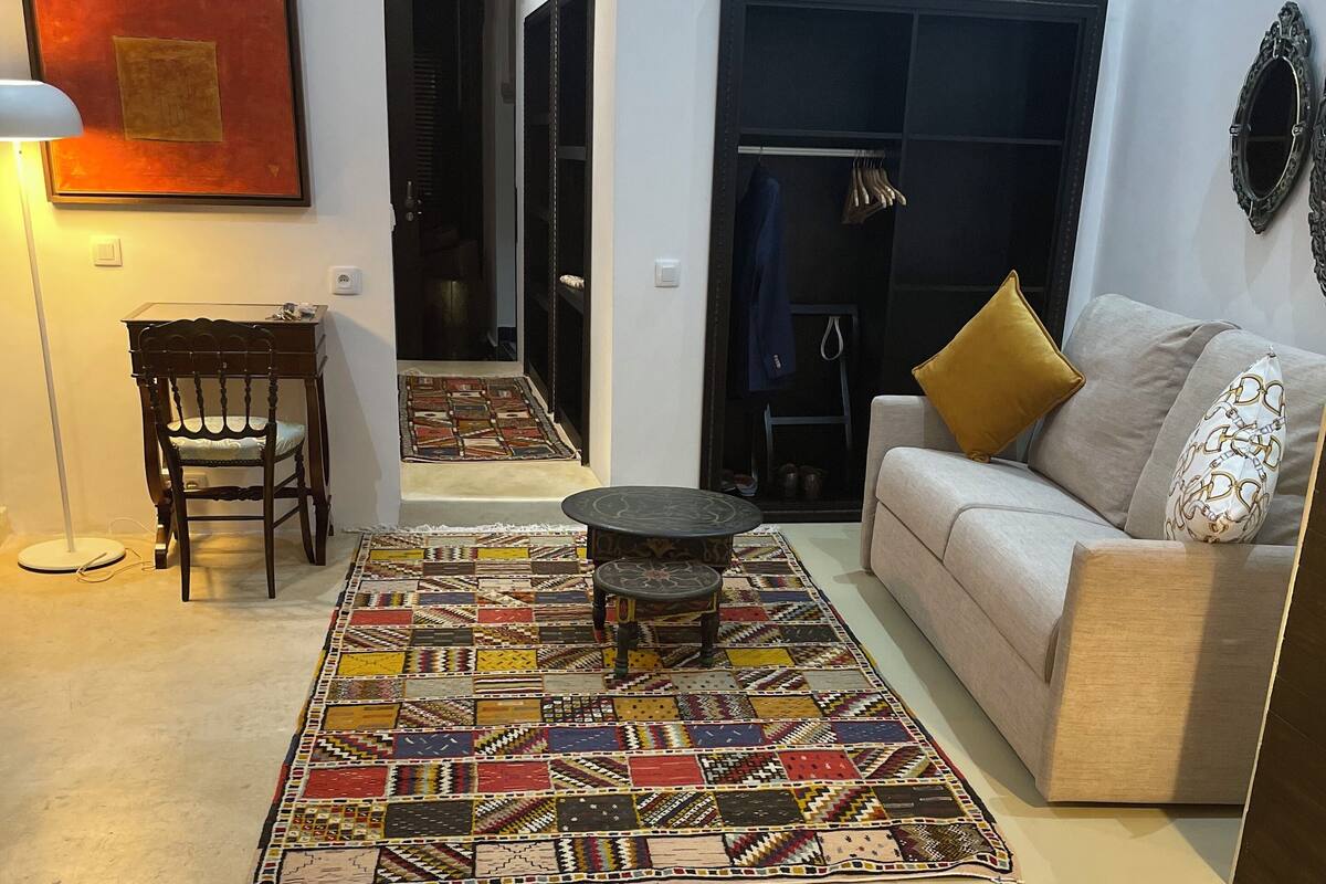 A living room with a patterned rug, a sofa with cushions, a wooden chair, and a small table.