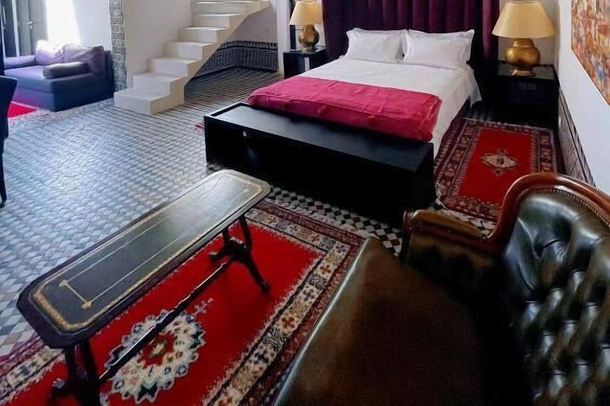 A bedroom with a bed, nightstands, a sofa, a chair, a table, and a staircase.