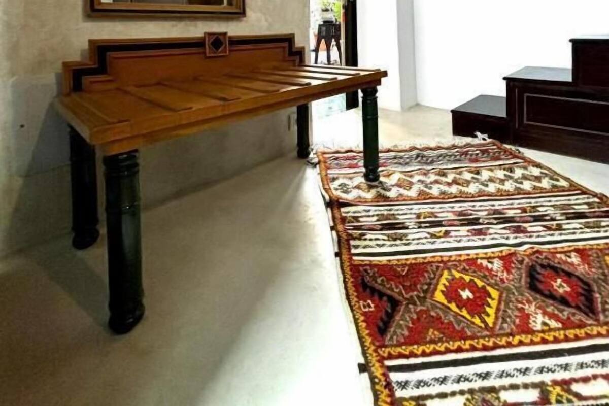 A room with a wooden bench, a mirror, a patterned rug, and a staircase leading to another area.