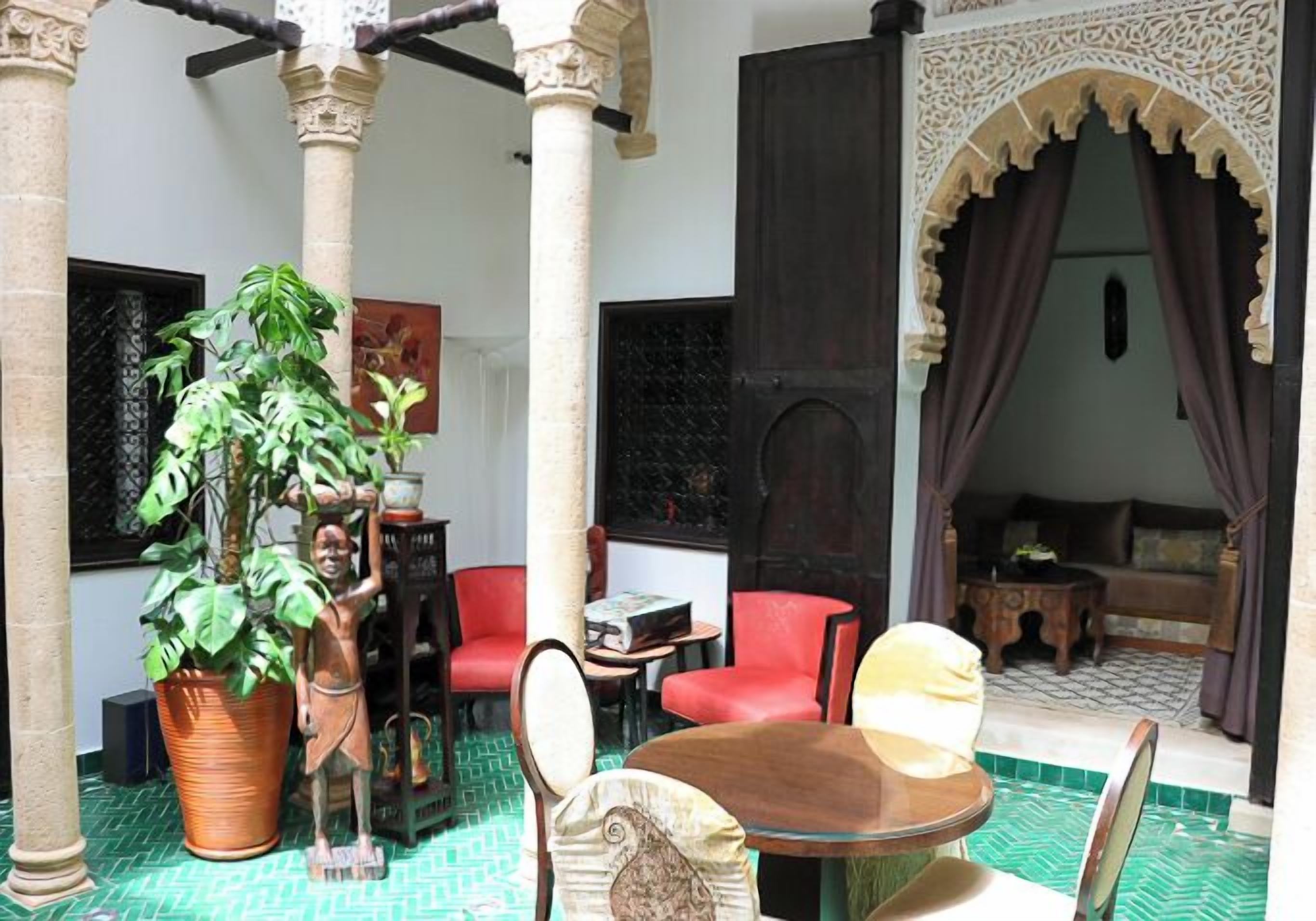 Ein traditionelles Interieur mit Fliesenboden, einer zentralen Sitzecke mit Tisch und Stühlen, einem Blumentopf und einem dekorativen Bogen.