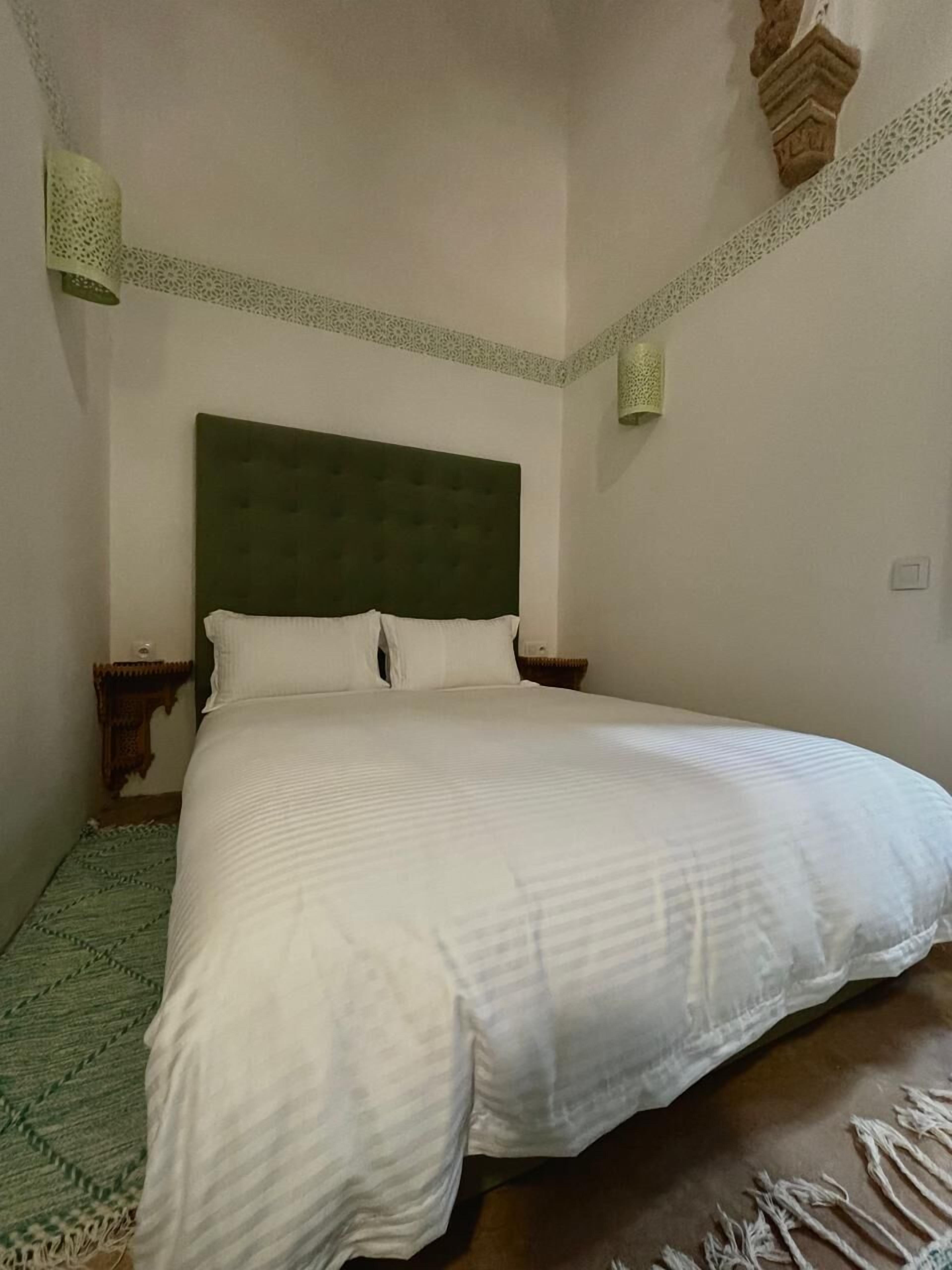A large bed with a green headboard, white bedding, and a patterned rug.
