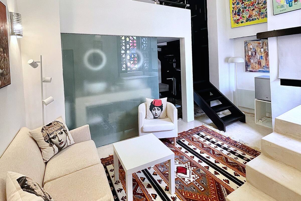 A modern living room with a sofa, a coffee table, and a patterned rug. There is a staircase leading to an upper level.