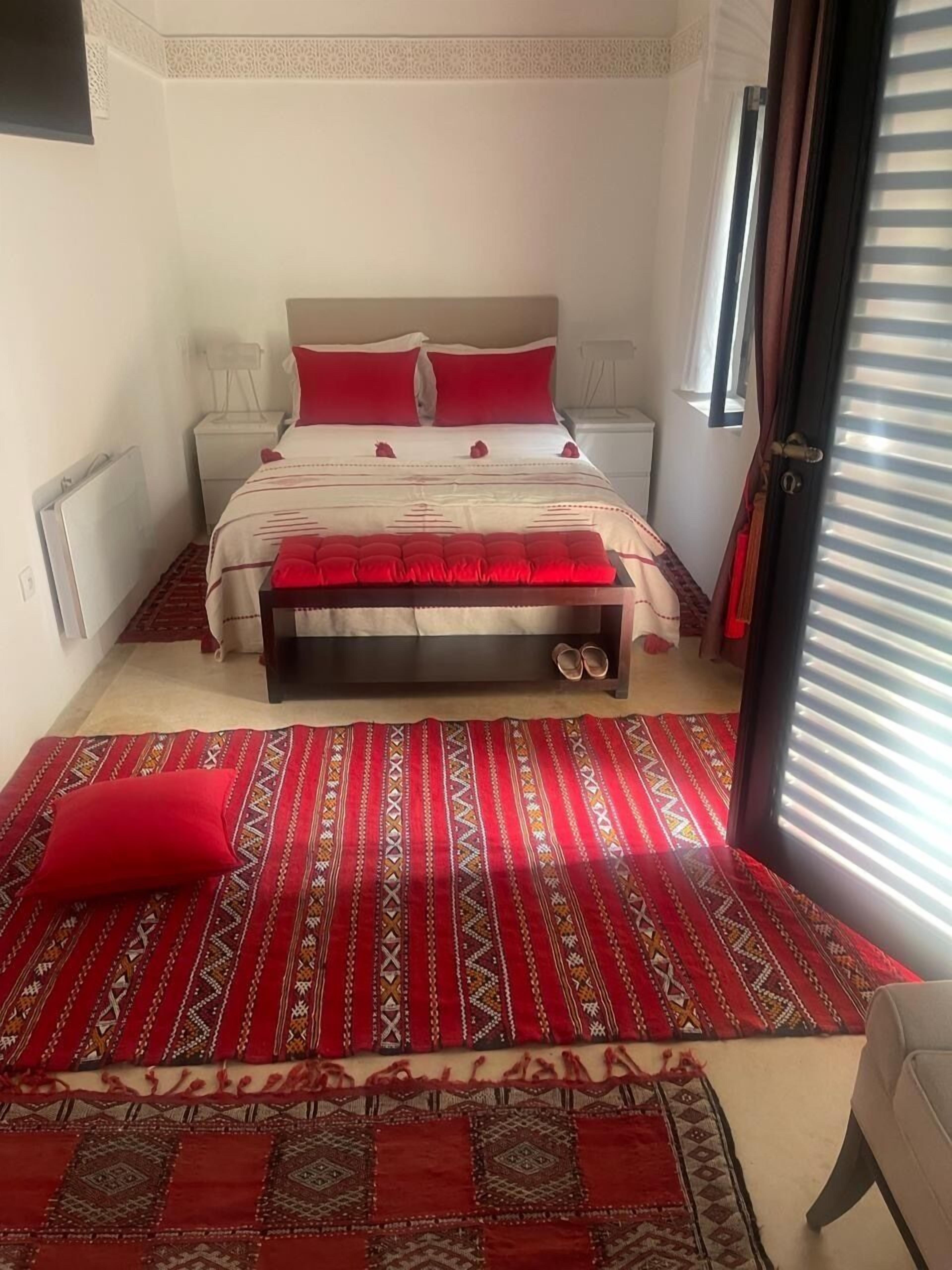 A bedroom with a bed, nightstands, a bench, and a patterned rug.