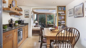 Una cocina con armarios de madera, una mesa de comedor con sillas y una estantería.