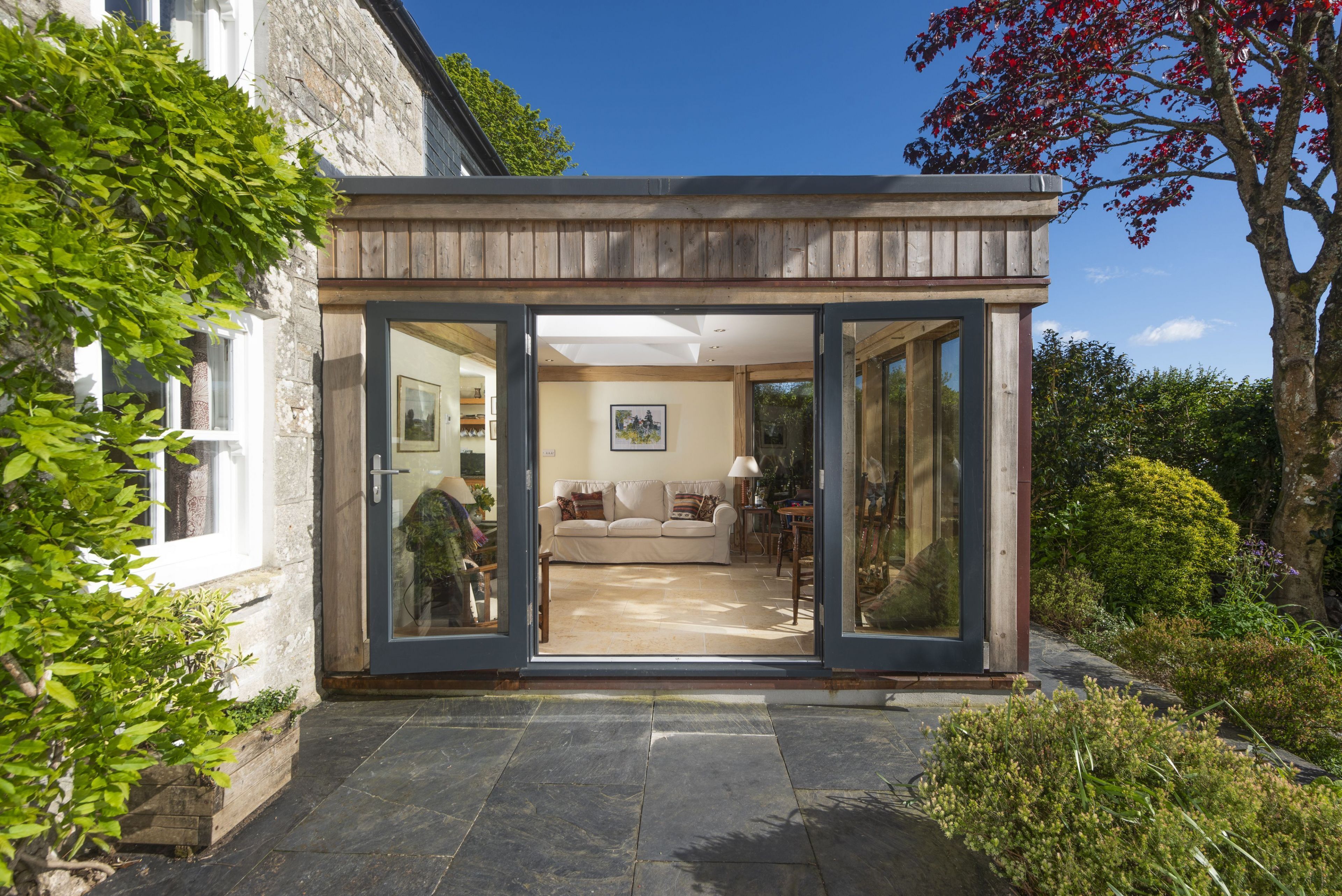 A modern house with a glass door leading to a living room with a sofa and a table.