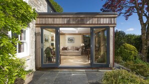 Una casa moderna con un puerta de cristal que da a una sala de estar con un sofá y una mesa.