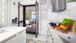 A modern kitchen with a stove, microwave, and a dining area with a view. - Villa Mapi (Massa Lubrense)