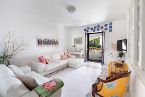 A living room with a white sofa, a coffee table, a TV, and a door leading outside.