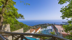 A pool area with a view of the sea, stone walls, and a wooden fence. - Villa Mapi (Massa Lubrense)