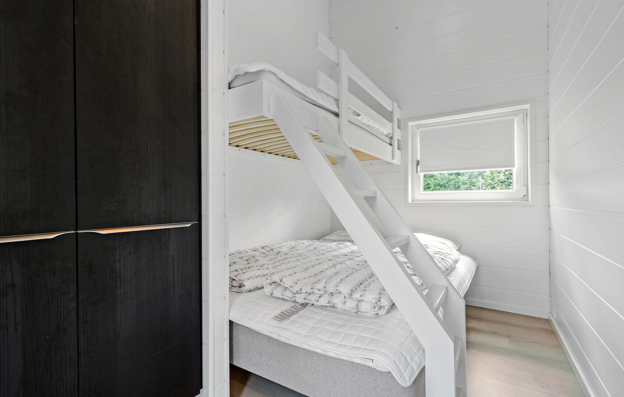 Una cama litera con escalera, una ventana con vistas y un armario de madera oscura.