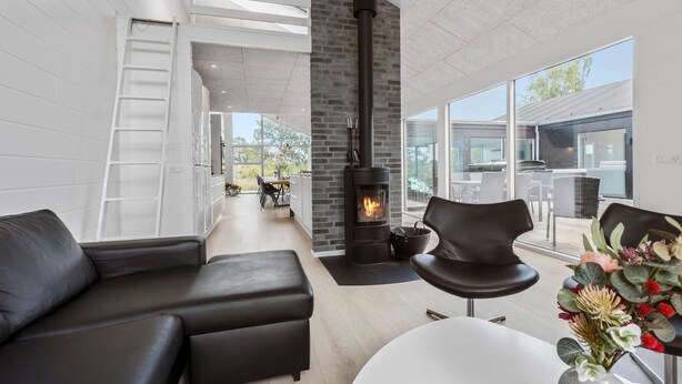 Una sala de estar moderna con una chimenea negra, un sofá blanco y un comedor con mobiliario de exterior.