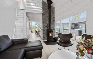 Un salon moderne avec une cheminée noire, un canapé blanc et un coin repas avec des sièges d’extérieur.