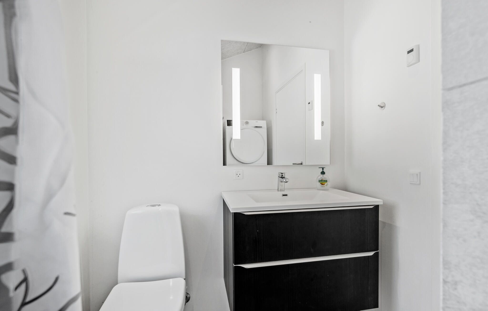 Ein Badezimmer mit weißem Waschbecken, schwarzem Waschtisch, einem Spiegel und einer Toilette.