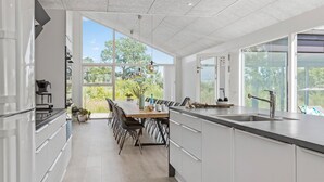 Una cocina moderna con armarios blancos, una isla grande con pileta y un comedor con mesa y sillas.