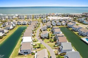 A residential area with houses, a canal, and a beach in the background. - My Happy Place by Brunswick Vacation Rentals: Cottage w/ Community Pool & Views (Ocean Isle Beach)