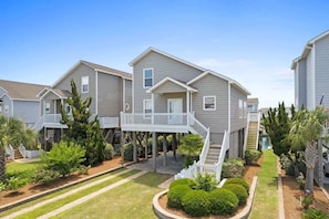 A residential building with a covered porch, a staircase, and a small garden area.