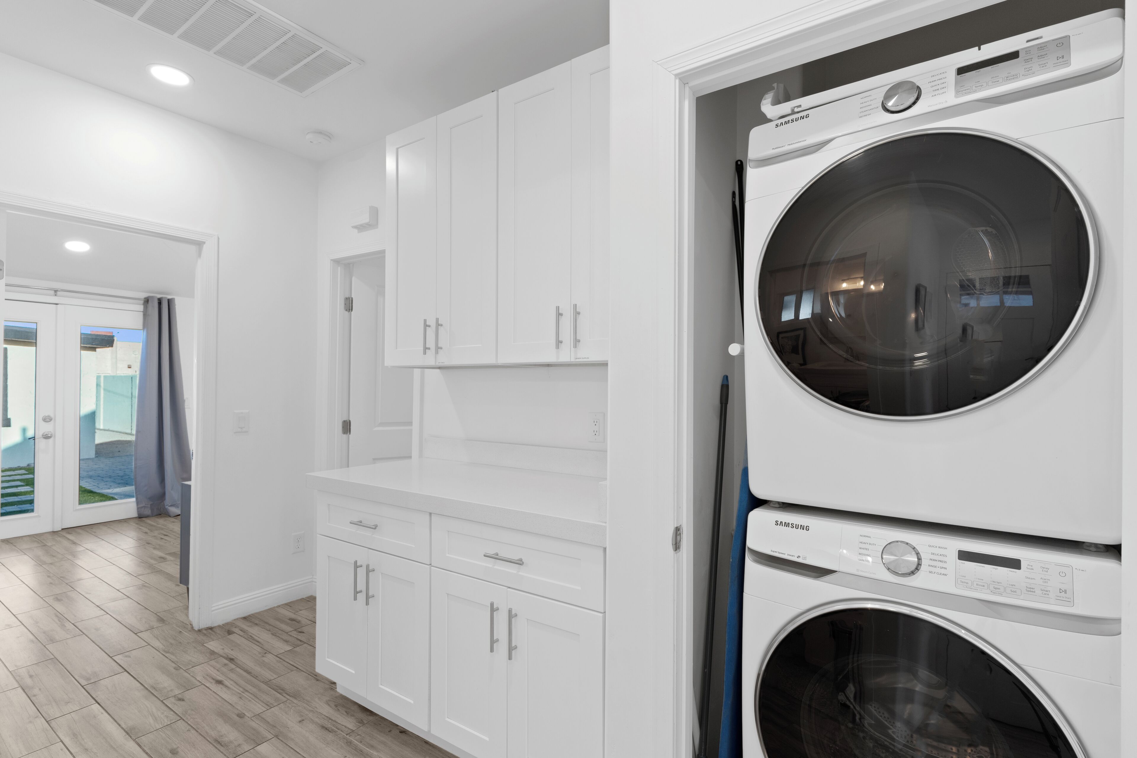 Un cuarto de lavandería con dos lavadoras apiladas, muebles blancos y piso de madera.
