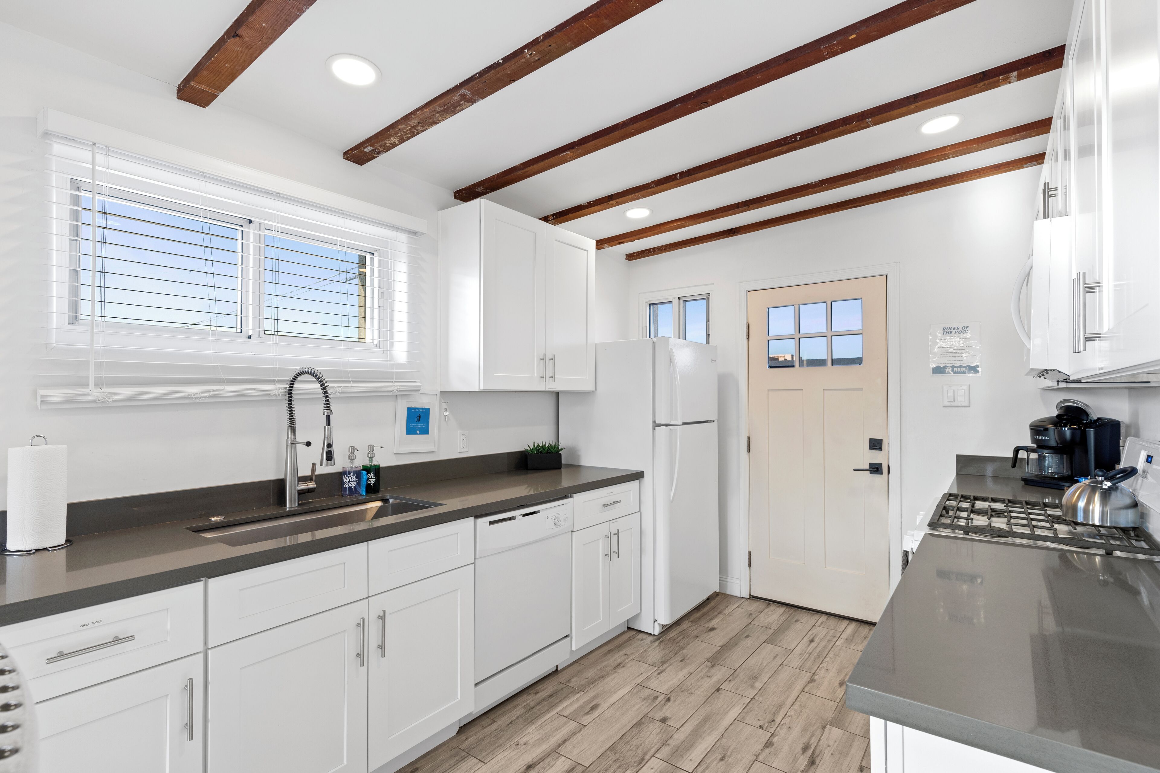 A modern kitchen with white cabinets, a stainless steel countertop, and a wooden ceiling.