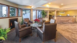 Eine Hotellobby mit Ledersesseln, einem runden Tisch mit Blumenvase, einem Kamin und einer Rezeption.
