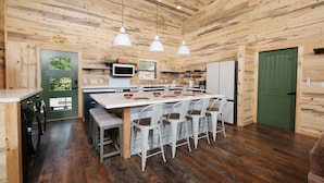 Interior de madera con zona de cocina que incluye una isla central con taburetes de bar, lavadora y una puerta verde.