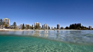 A beachfront hotel with clear waters, a sandy beach, and a city skyline in the background. - Rainbow Pacific Ocean Views (Coolangatta)