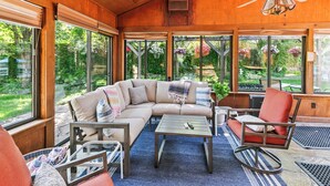 Un espacio interior acogedor con un amplio sofá modular, un sillón mecedora y una mesa de centro. Amplias ventanas ofrecen vistas al jardín.