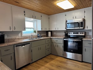 A modern kitchen with white cabinets, stainless steel appliances, and a wooden ceiling.