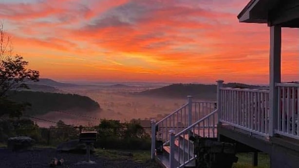 Ett hus med en veranda och en trappa som leder upp till en terrass, med utsikt över en dal och en himmel i solnedgång.