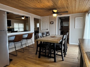 A modern kitchen with wooden flooring, a dining table with chairs, a ceiling fan, and a refrigerator.